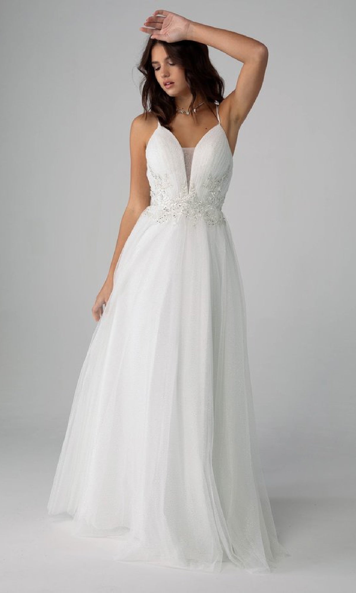Woman wearing the Lace-Up Long Shimmer Prom Dress Eureka 9797, featuring a lace bodice and flowing tulle skirt, standing against a plain gray background.